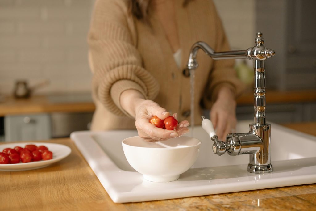 woman washing tomatoes in a kitchen sink